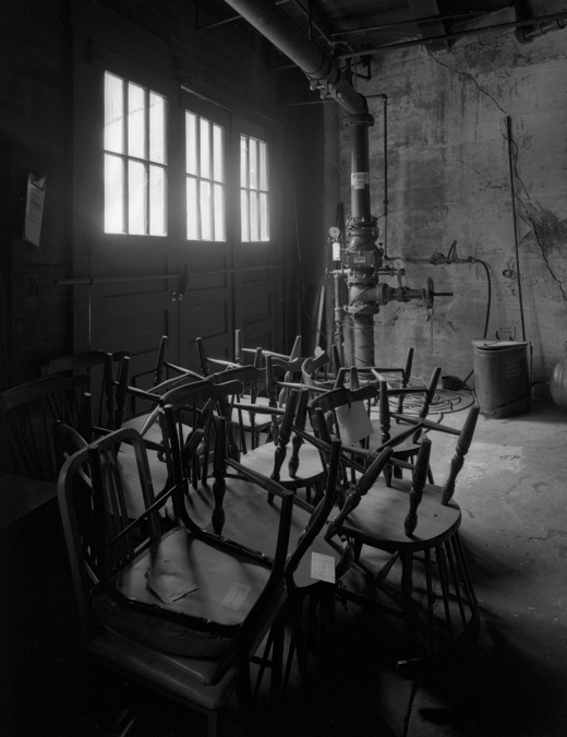A stack of broken and unused chairs sits in the boiler room. This photograph was a two-and-a-half minute long exposure made with available light.